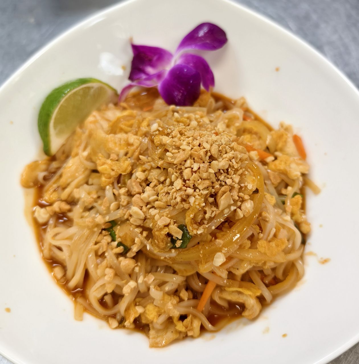 Our pad thai — rice noodles, crushed peanuts, lime, and orchid garnish, plated in the Wheat Ridge kitchen